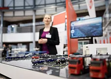 Eine Frau präsentiert ein Modell mit Autos und Lkw an einem Ausstellungsstand.