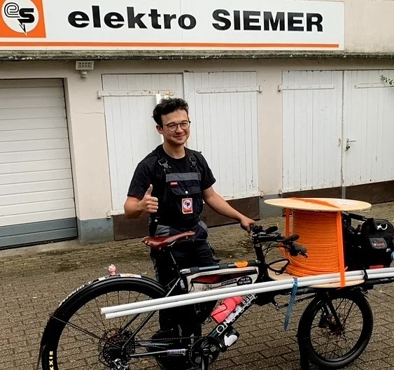 Ein Mitarbeiter der elektro SIEMER GmbH steht mit einem Lastenrad vor dem Firmengebäude .