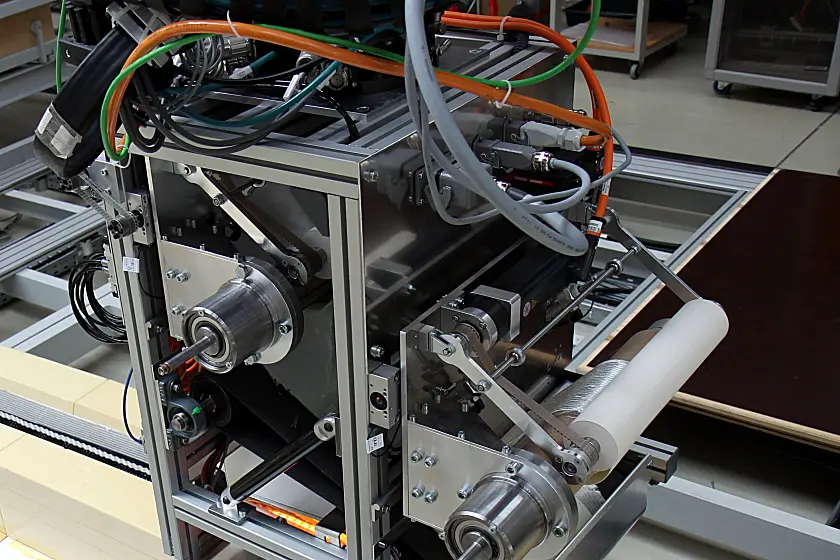 Industrielle Maschine mit Metallrahmen, Antriebsrollen, Riemen, Sensoren und Kabeln.